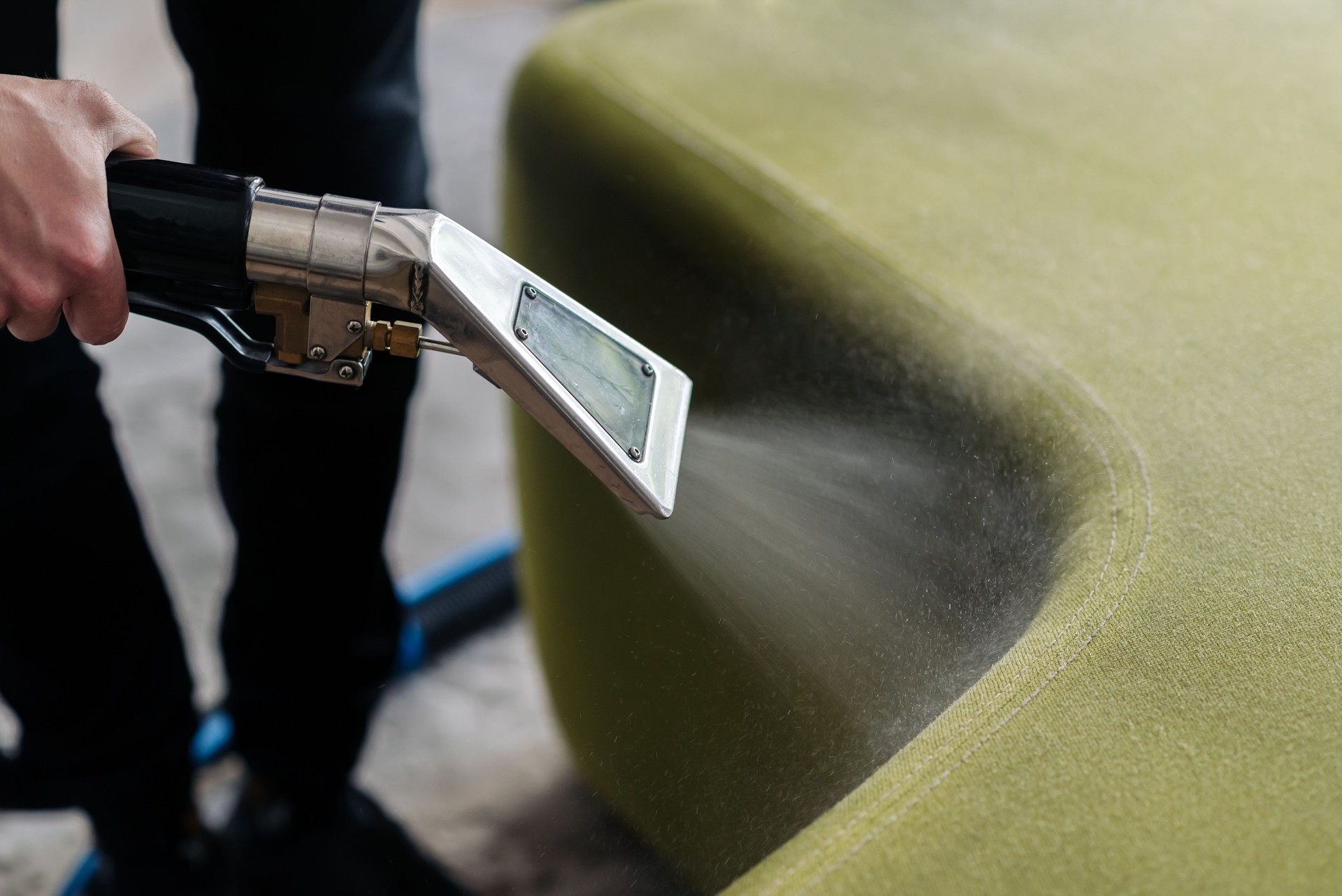 Close-up of housekeeper holding modern washing vacuum cleaner and cleaning dirty sofa with stain with professionally detergent. Professional spring clean at home concept